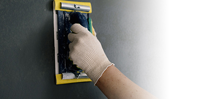 Hand in glove applying spackle on wall
